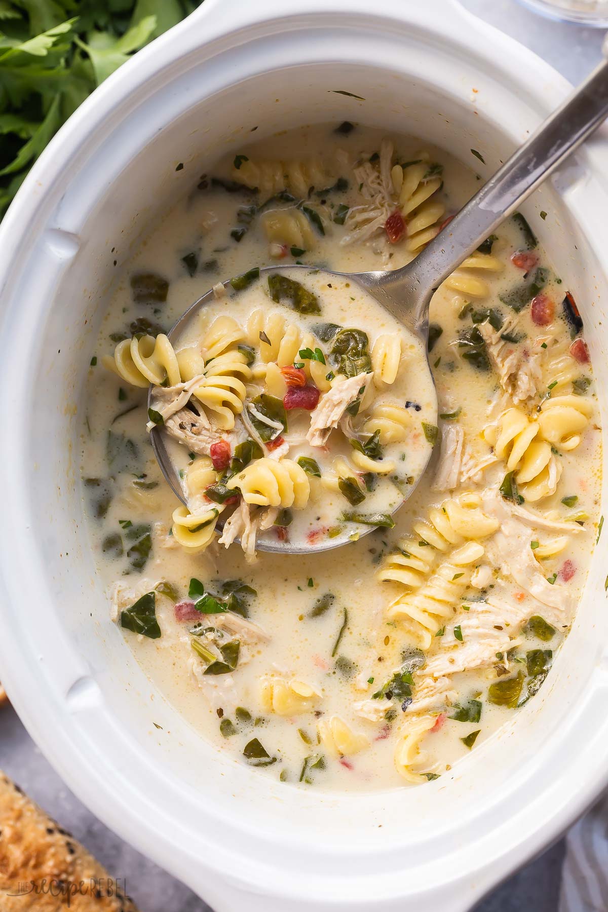 metal ladle scooping creamy italian chicken noodle soup out of white slow cooker.