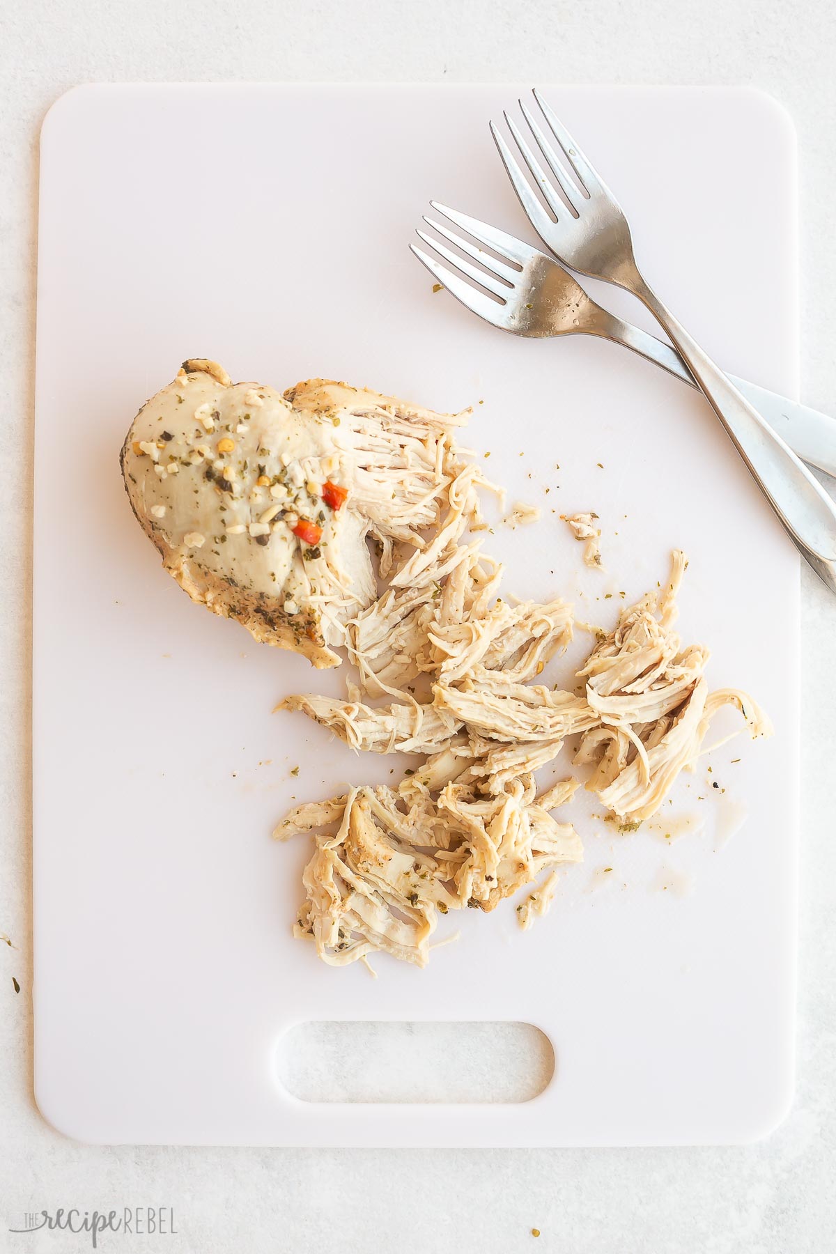 chicken breast on white cutting board being shredded with two forks.