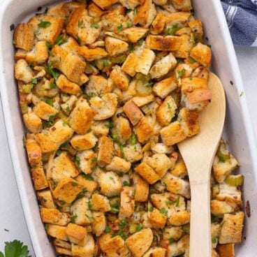 overhead image of stuffing in white backing dish with wooden spoon.