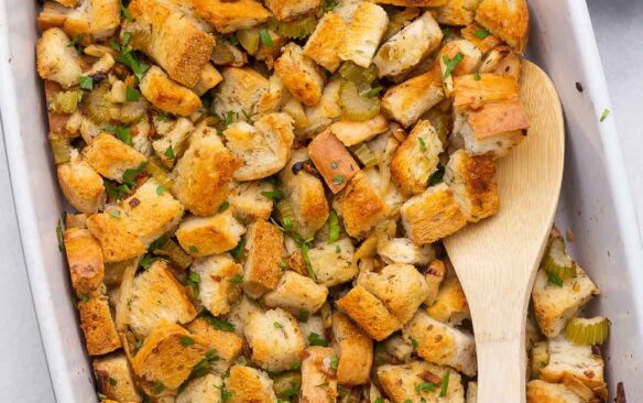 overhead image of stuffing in white backing dish with wooden spoon.