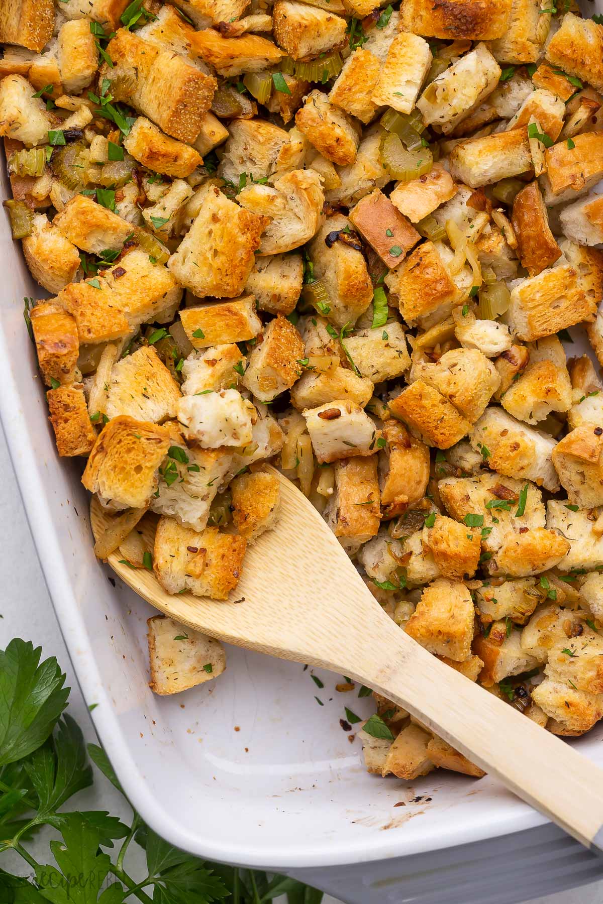 wooden spoon scooping stuffing from baking dish.