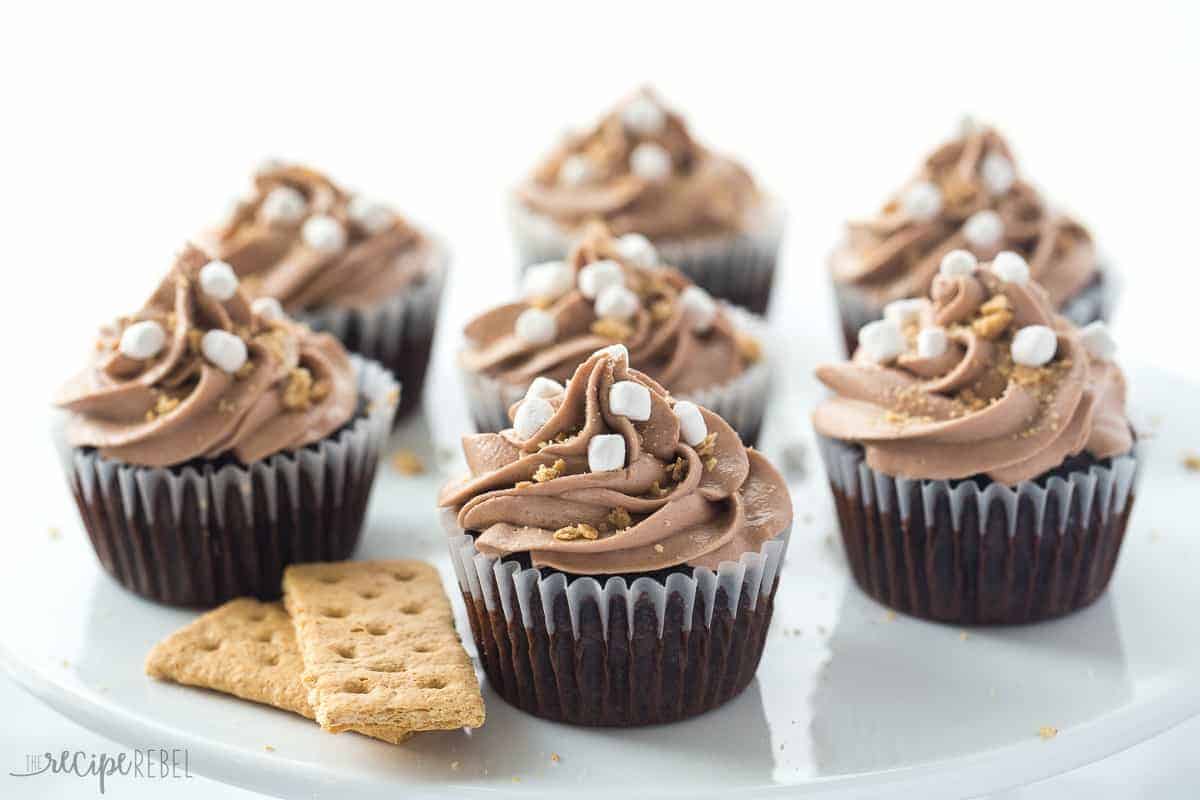 nutella smores cupcakess on white cake plate with crushed graham crackers and mini marshmallow bits