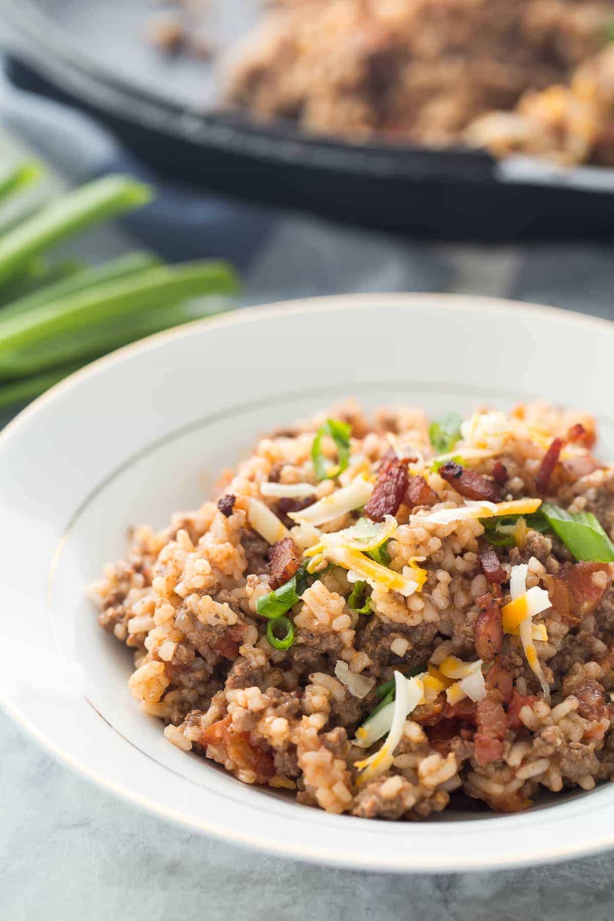 white bowl with bacon cheeseburger rice topped with shredded cheddar cheese and green onions