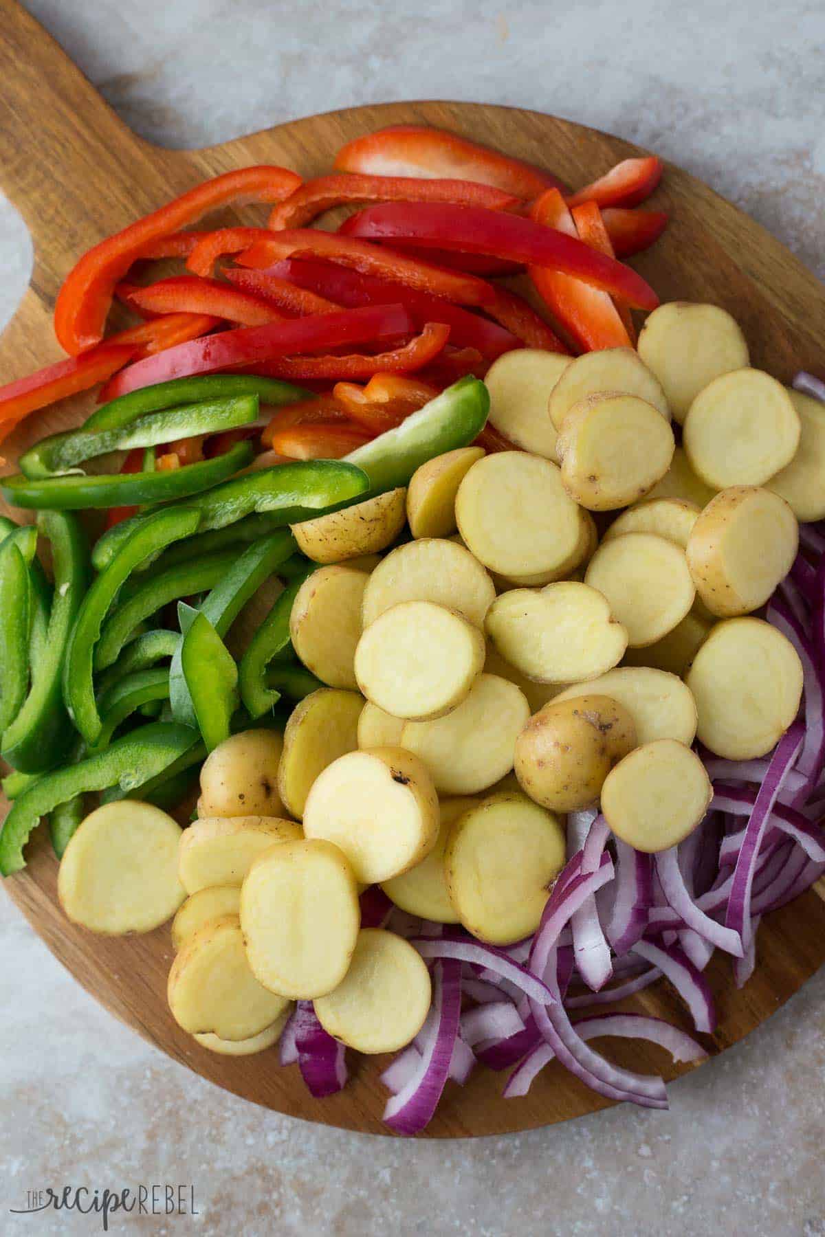 sliced red and green peppers sliced red onions and sliced potatoes raw on a cutting board