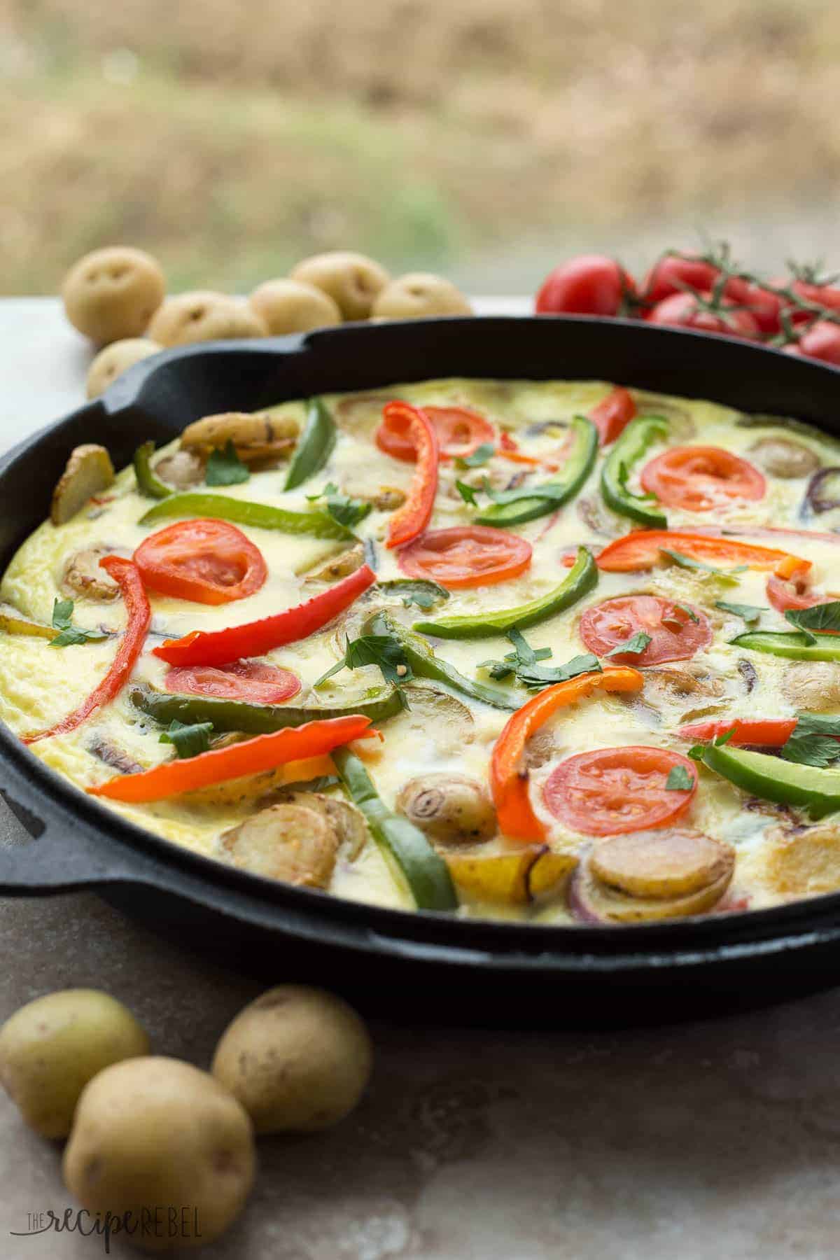 spanish tortilla in black cast iron skillet with potatoes and sliced peppers and tomatoes