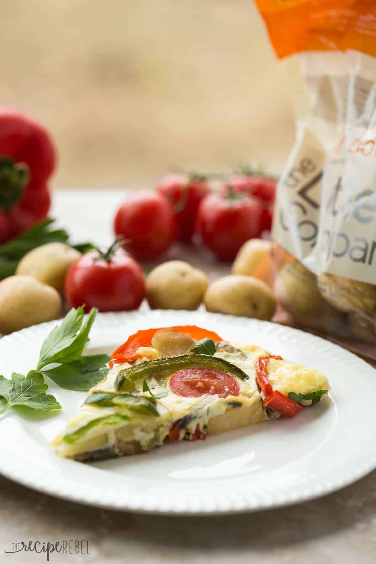 slice of spanish tortilla on white plate with bag of little potatoes behind