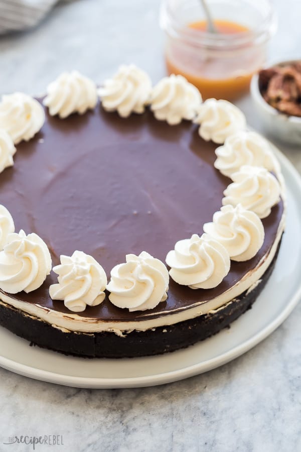 This NO BAKE Turtle Cheesecake is made with a chocolate cookie crust, salted caramel pecan layer, luscious cheesecake layer and a thin layer of chocolate ganache. Top it with whipped cream, caramel and pecans for a decadent treat! #cheesecake #turtle #caramel #chocolate no bake turtle cheesecake whole with chocolate ganache and whipped cream