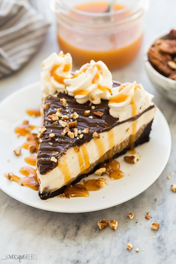 turtle cheesecake on plate with caramel drizzle, pecans and whipped cream
