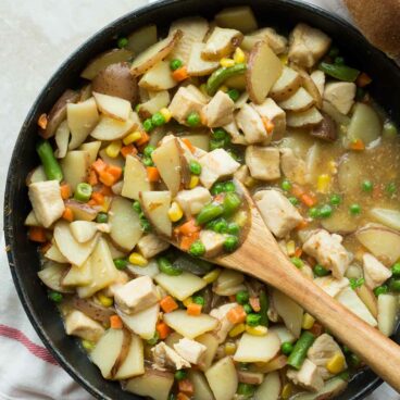 30 minute skillet chicken stew in large black skillet with wooden spoon scooping