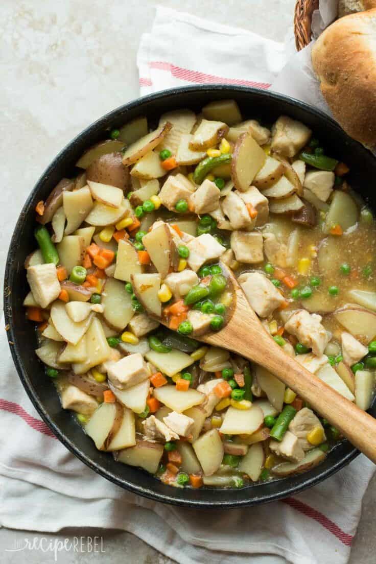 30 minute skillet chicken stew in large black skillet with wooden spoon scooping