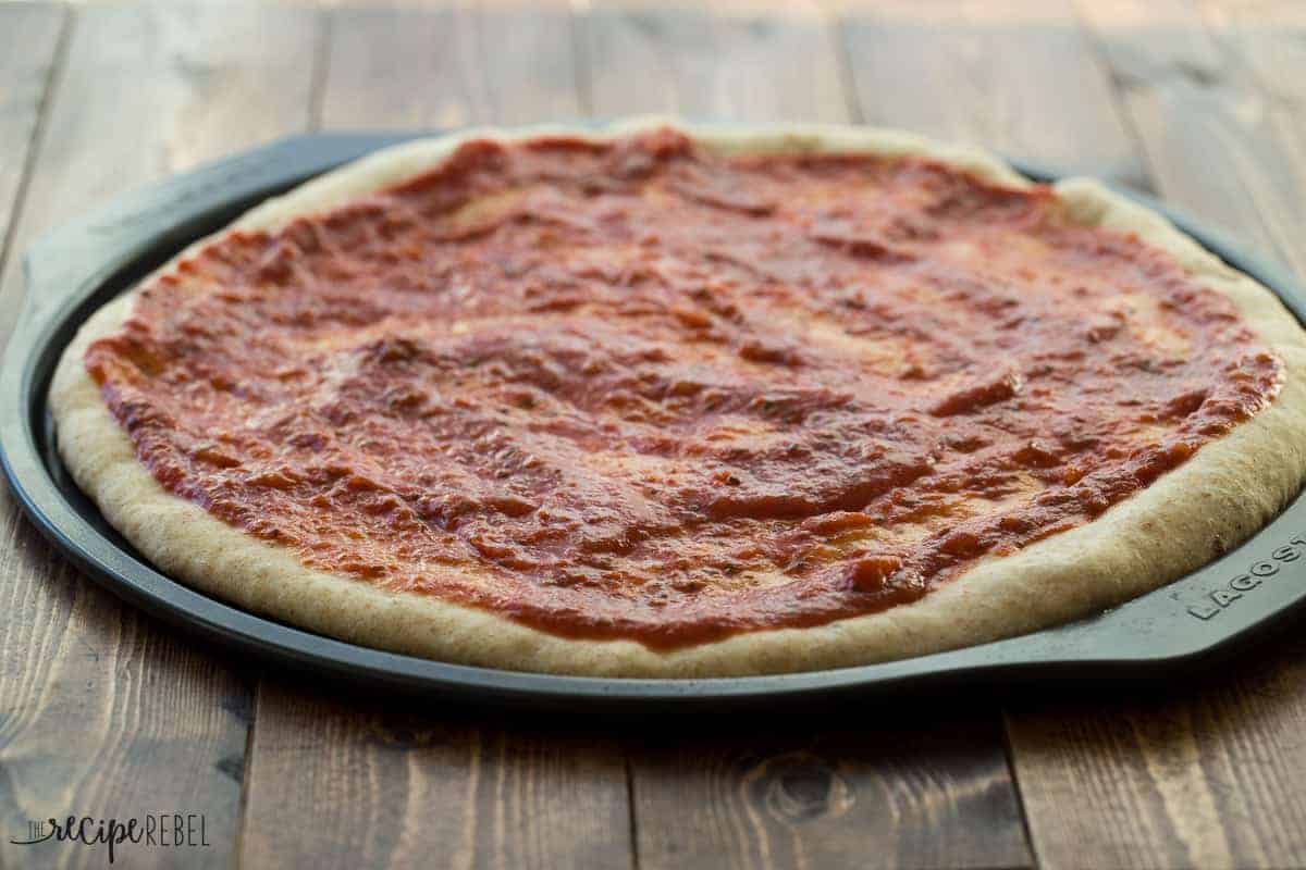 par baked pizza dough on pizza pan covered in tomato sauce