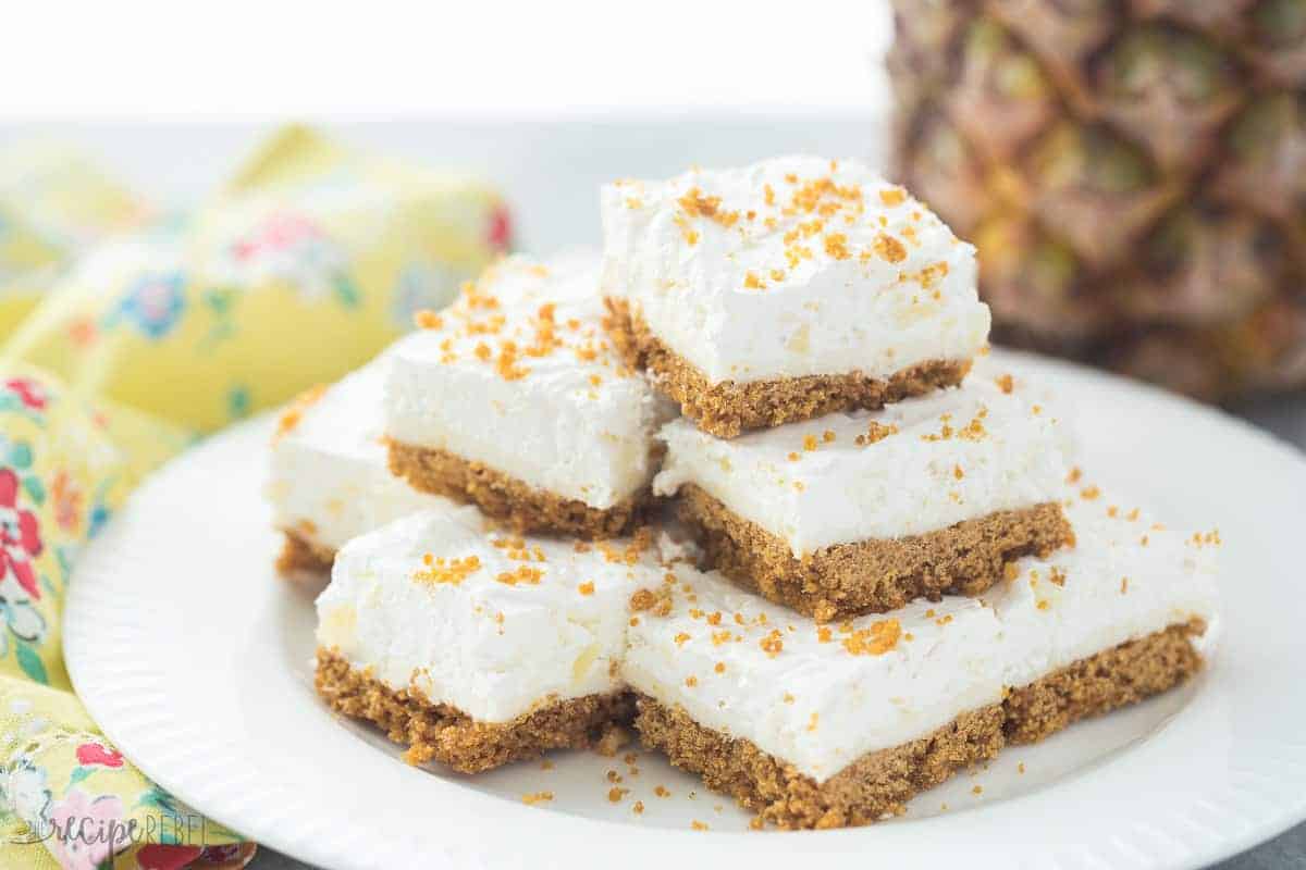 almost no bake pineapple squares stacked on white plate with crushed graham crumbs on top