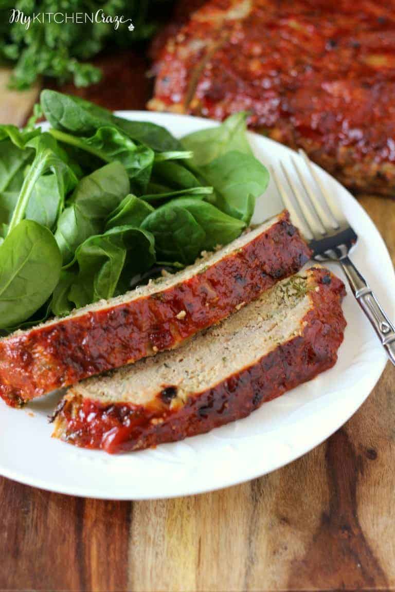 glqzed meatloaf two slices on white plate with fresh spinach