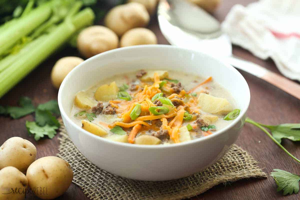 white bowl with cheeseburger soup and potatoes and celery in the background
