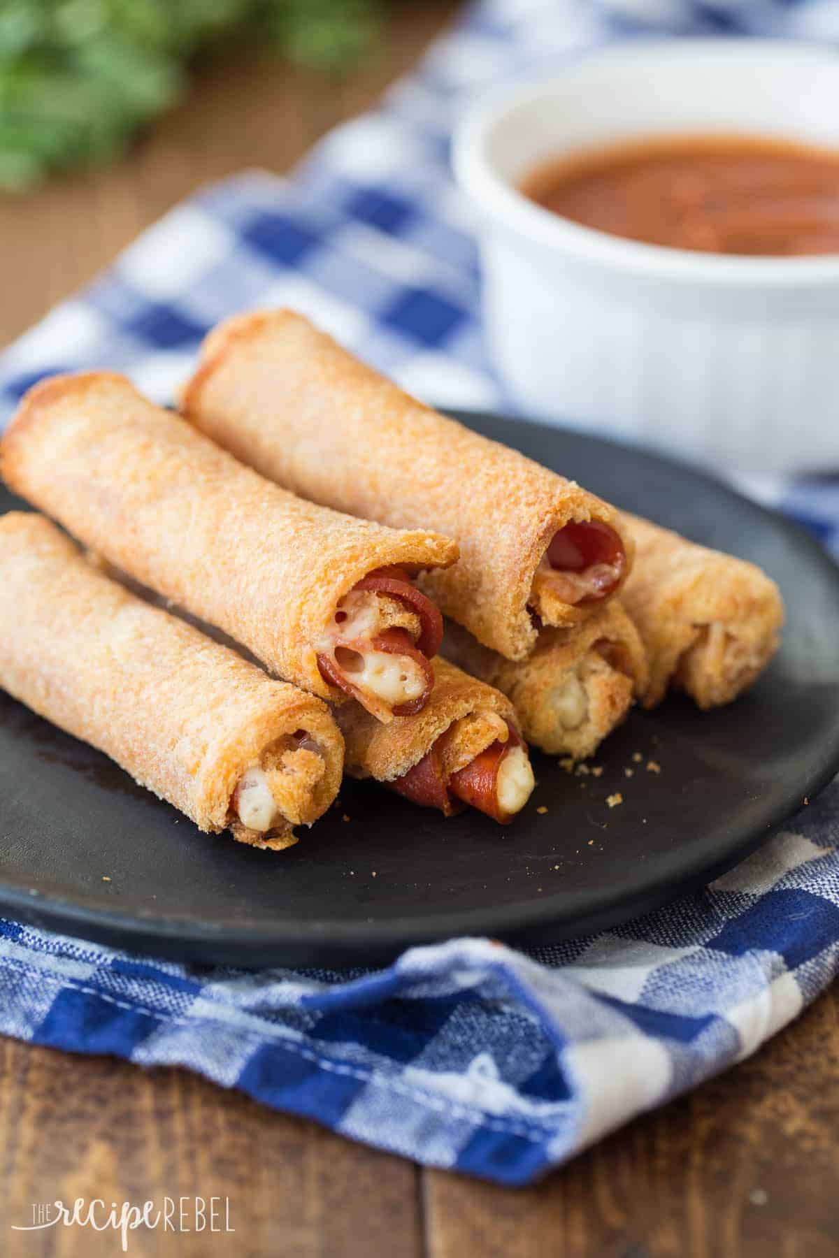 6 pizza roll ups stacked on black plate on top of blue checkered napkin