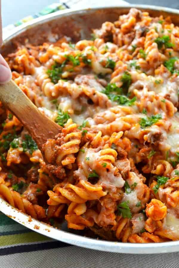 skillet cheesy beef ziti close up image with wooden spoon lifting pasta