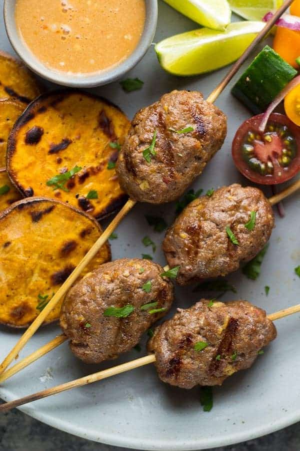 thai curry beef koftas close up on grey plate with cherry tomatoes and grilled sweet potatoes