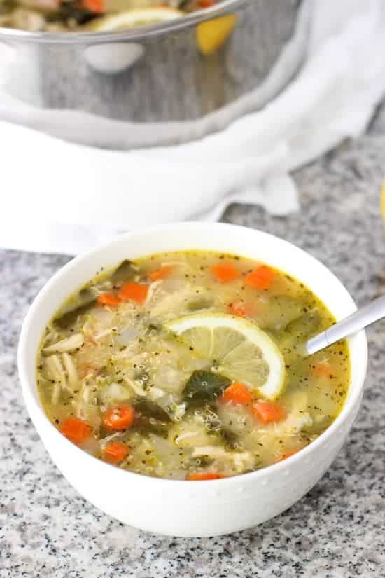 lemon quinoa chicken soup with spinach in white bowl with grey background
