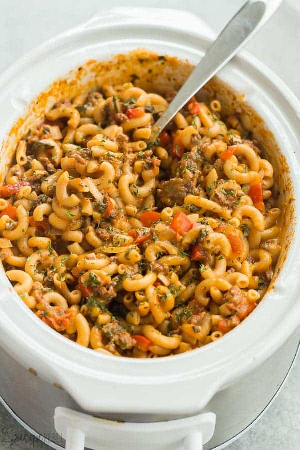 hamburger helper recipe in white slow cooker on grey background with metal spoon stuck in