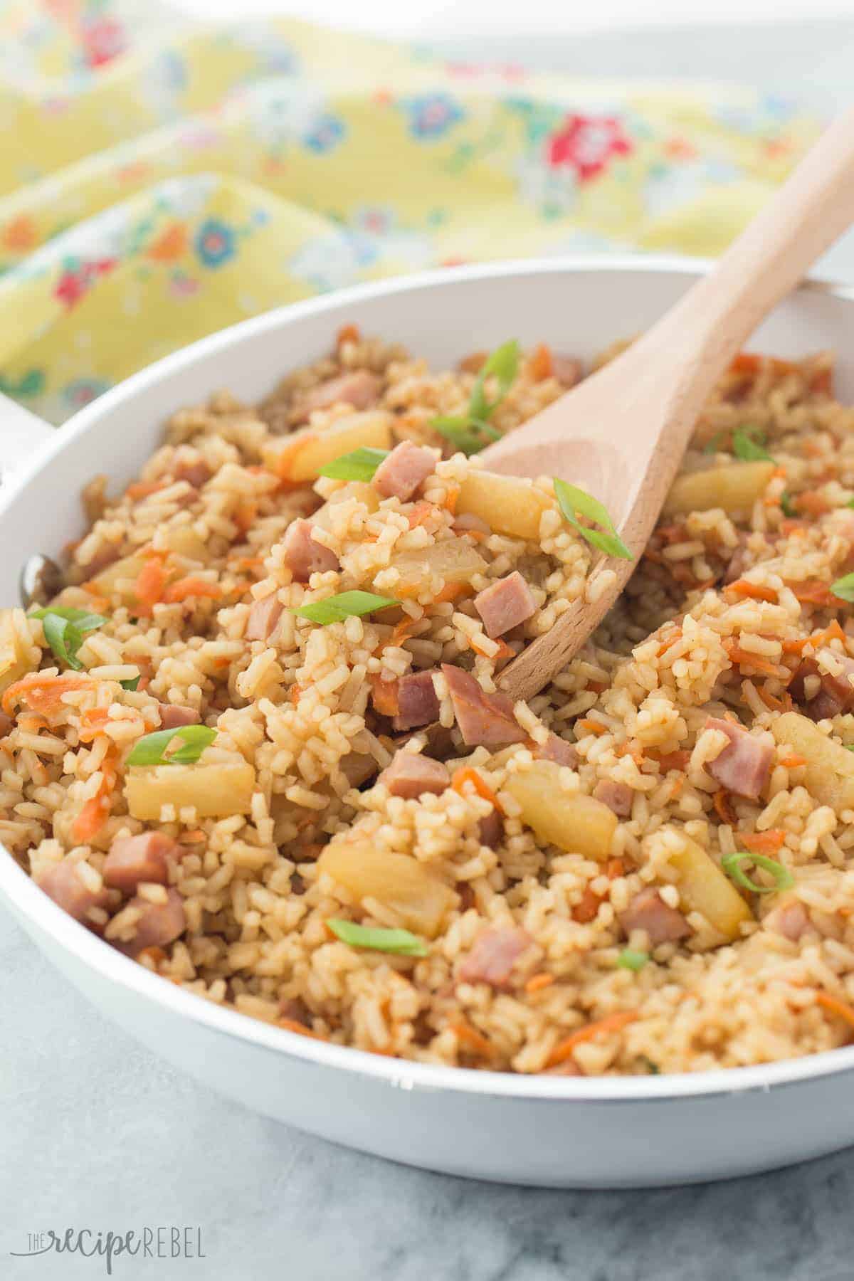 ham and pineapple rice in white skillet with wooden spoon stuck in rice