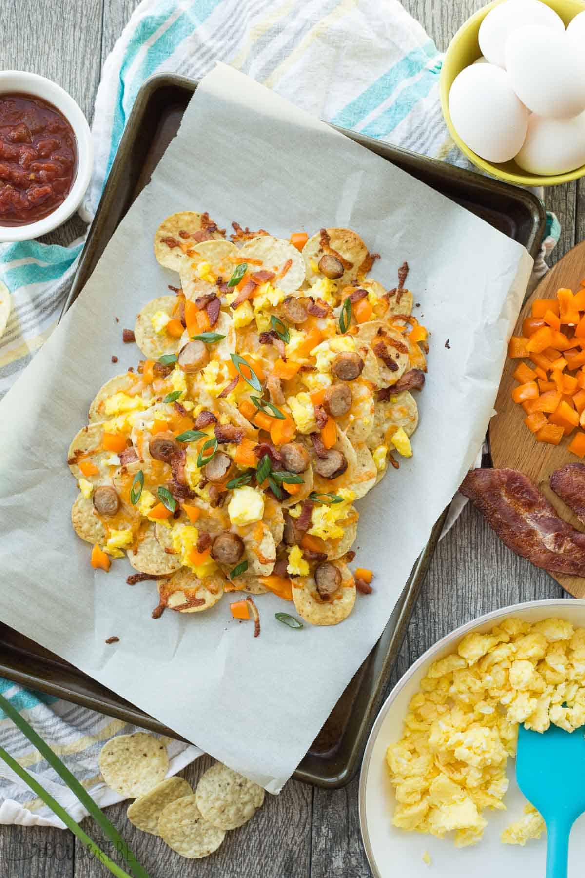 overhead image of ingredients of breakfast nachos with pan of nachos including eggs peppers bacon