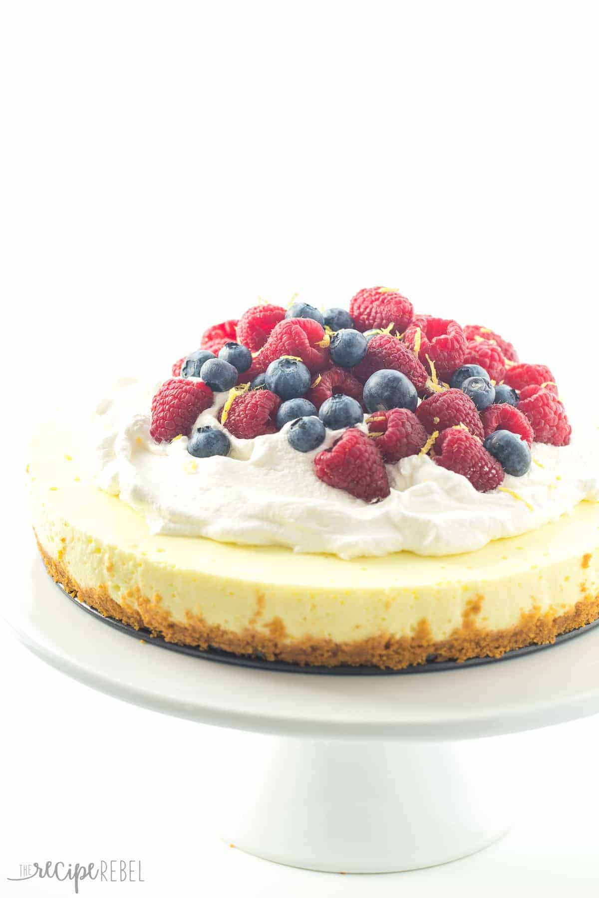 A light, luscious, no bake Lemon Cheesecake with a secret ingredient that makes it even healthier! Top with whipped cream and fresh berries for the perfect Spring or Easter dessert. light no bake cheesecake on a white cake plate piled with berries