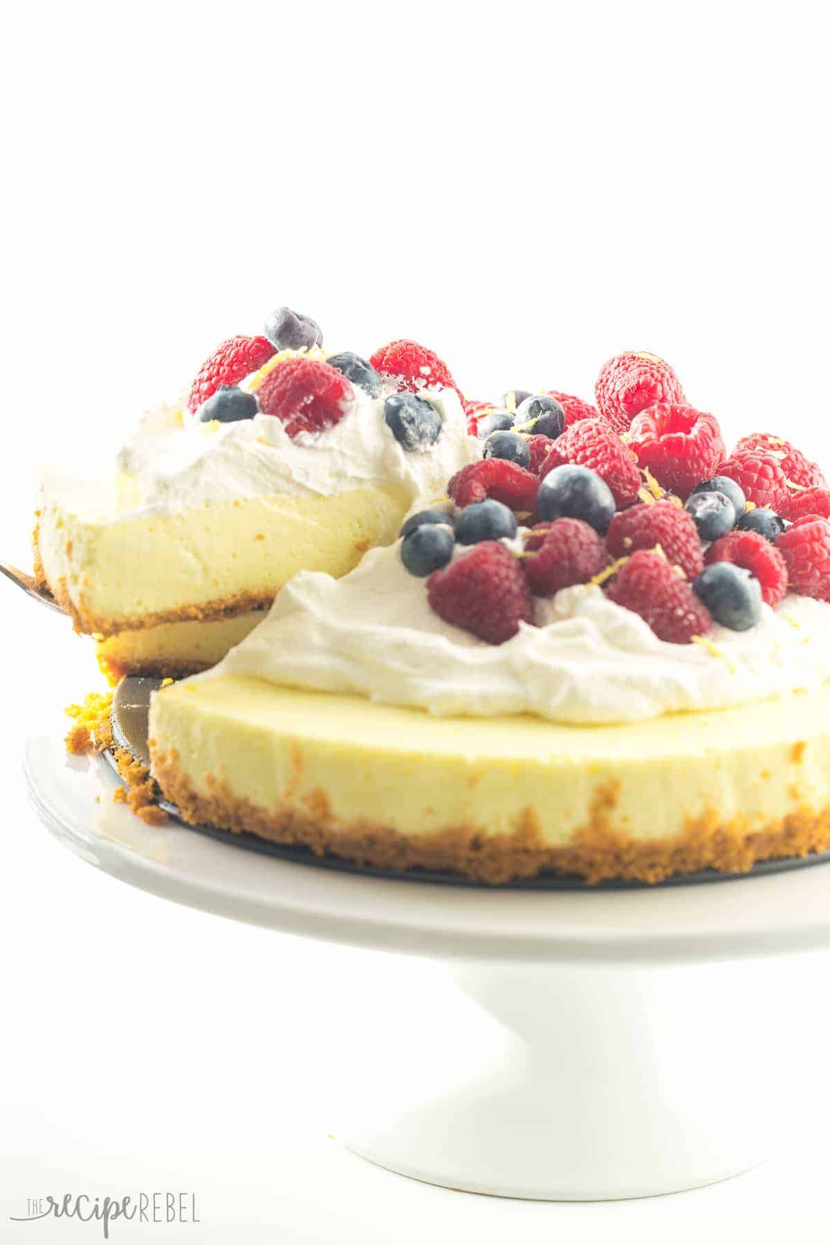 piece being removed from light lemon cheesecake with whipped cream and berries on top