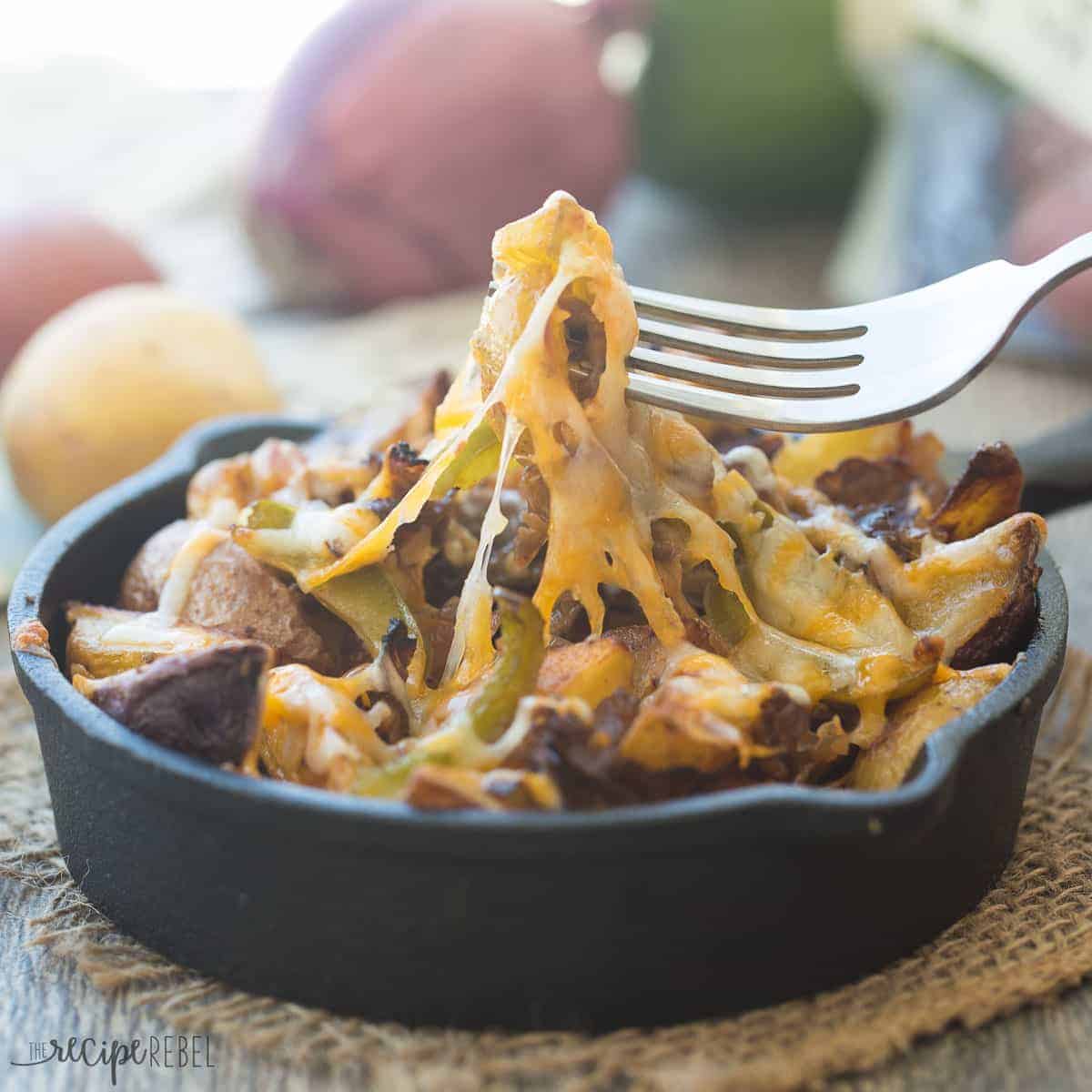 mini cast iron skillet with philly cheesesteak potato wedges with fork pulling some up