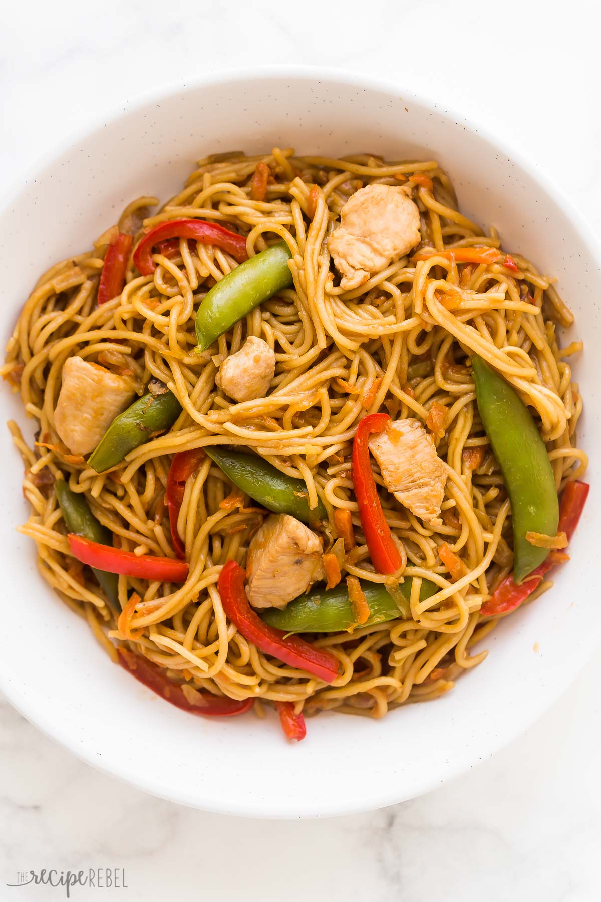 overhead image of bowl of chicken chow mein with snap peas and peppers