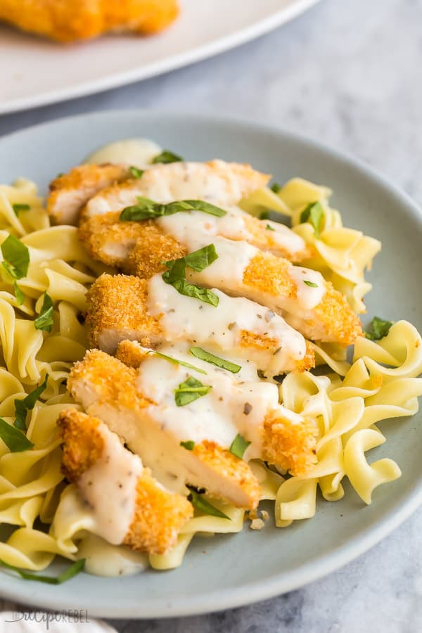 close up image of crispy chicken sliced over egg noodles on grey plate