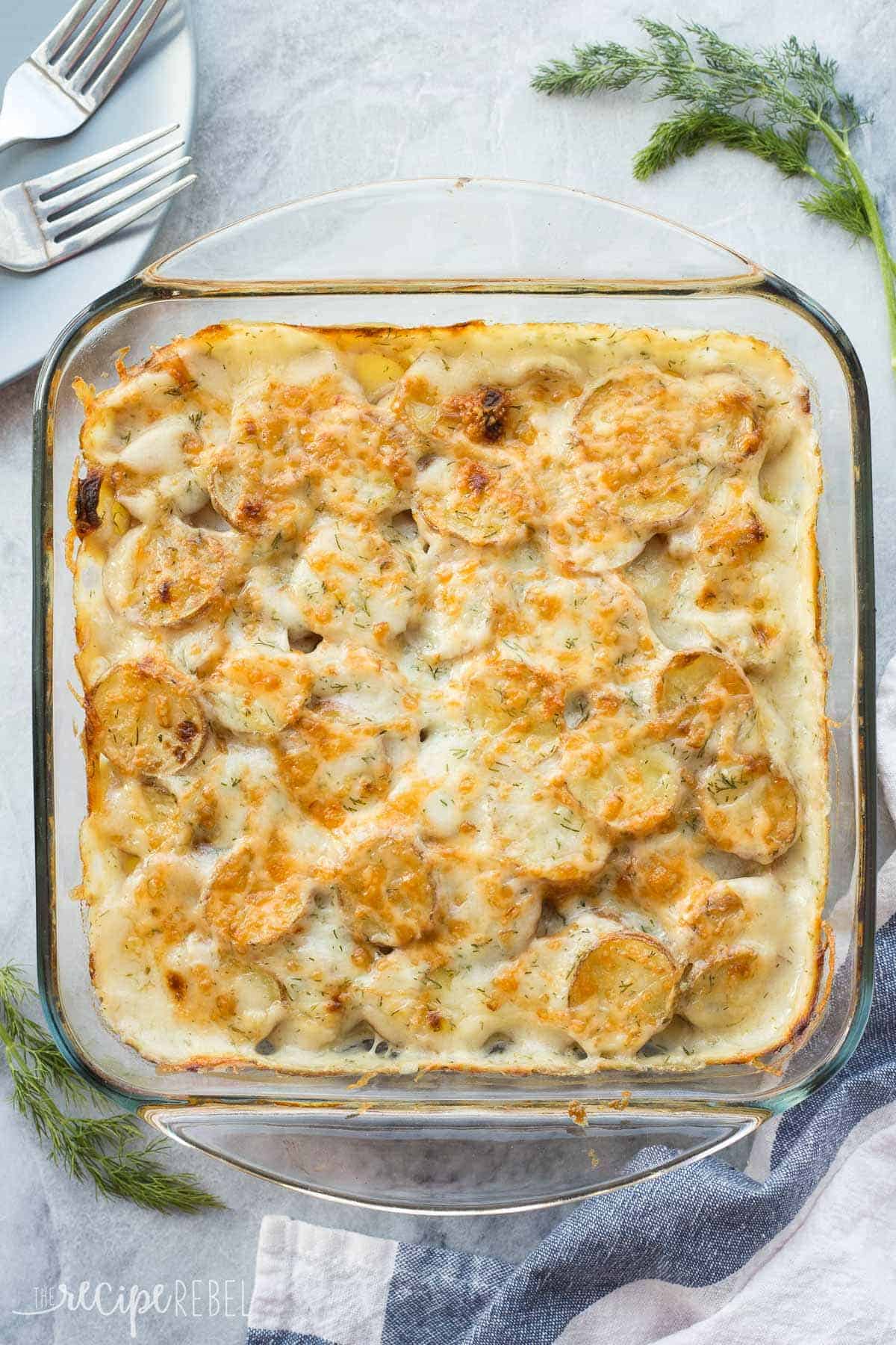 overhead image of dill scalloped potatoes in glass baking dish on grey marble