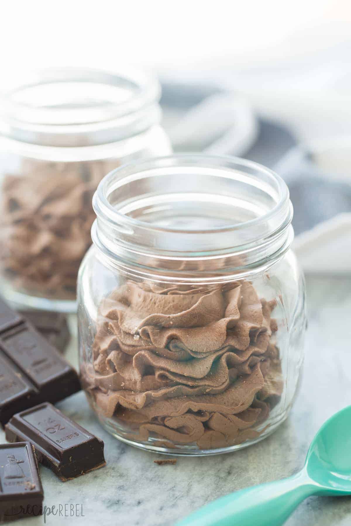 small mason jar with chocolate mousse inside and chocolate squares in the background