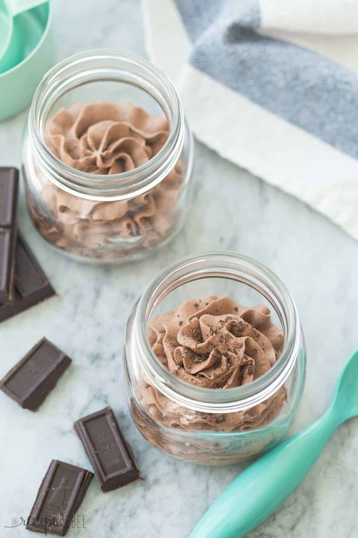 two small jars of chocolate mousse on grey marble with chocolate squares on the side