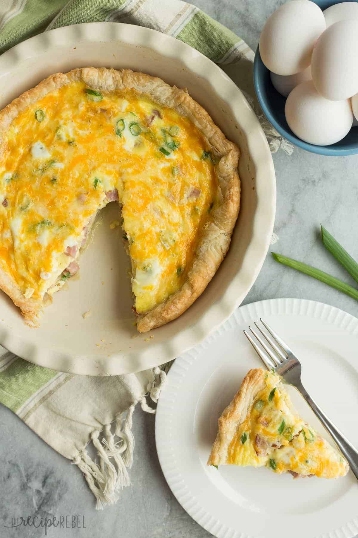 overhead image of puff pastry quiche with one piece cut out on white plate with eggs on the side