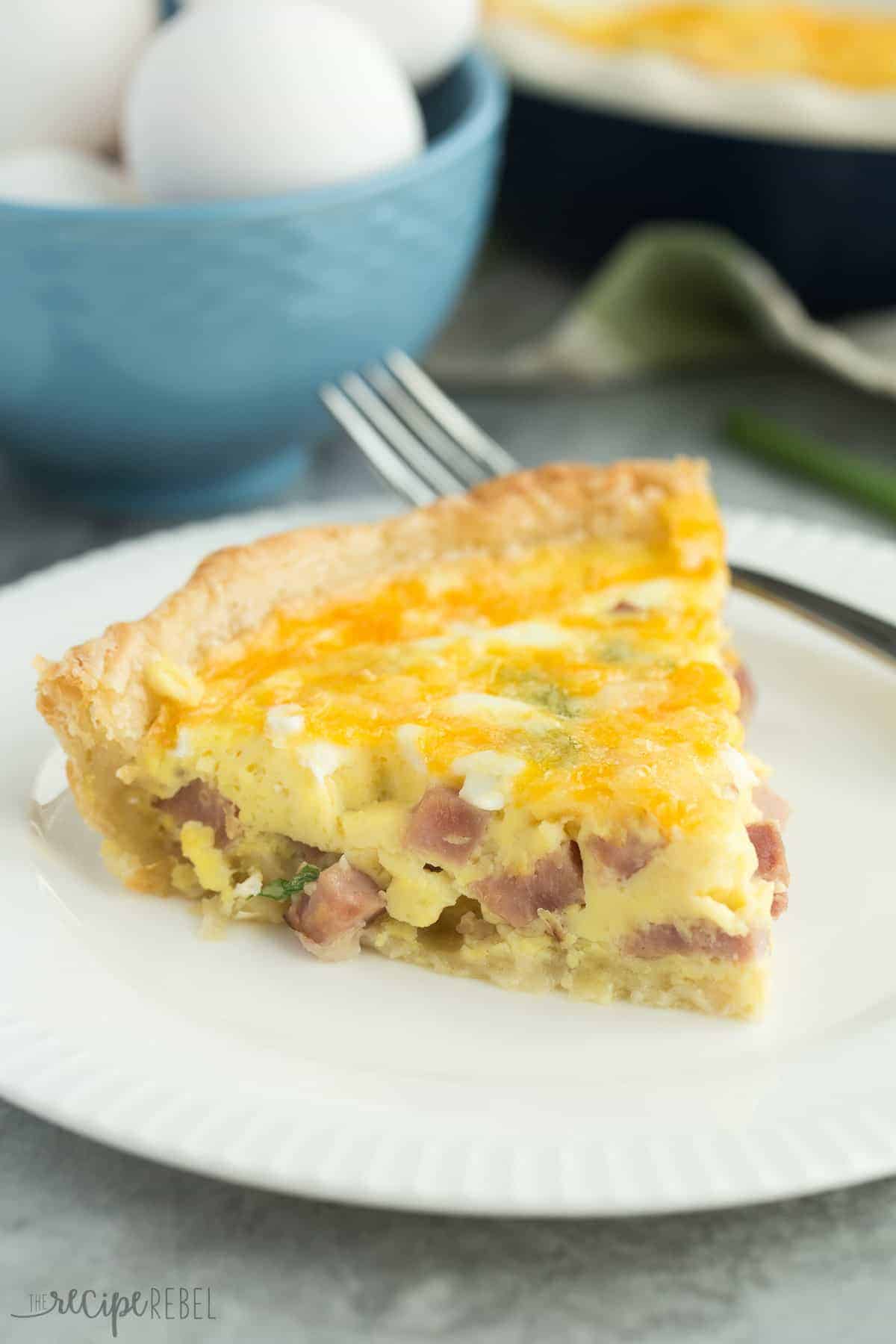 piece of puff pastry quiche on white plate with fork behind