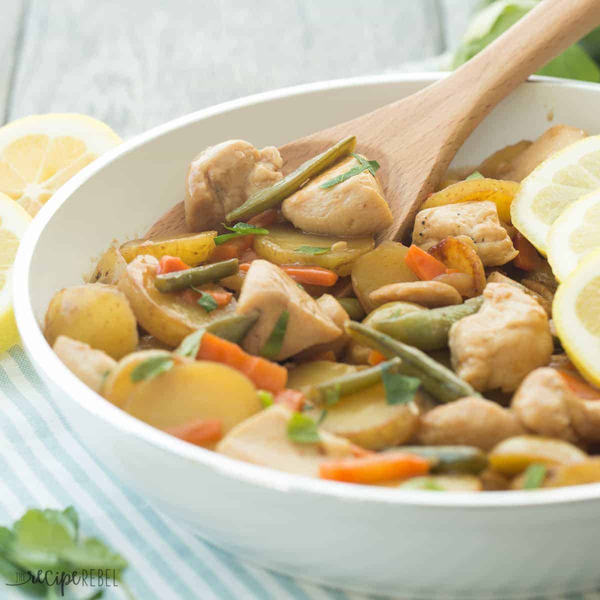 white skillet with honey lemon chicken and potatoes with green beans and carrots