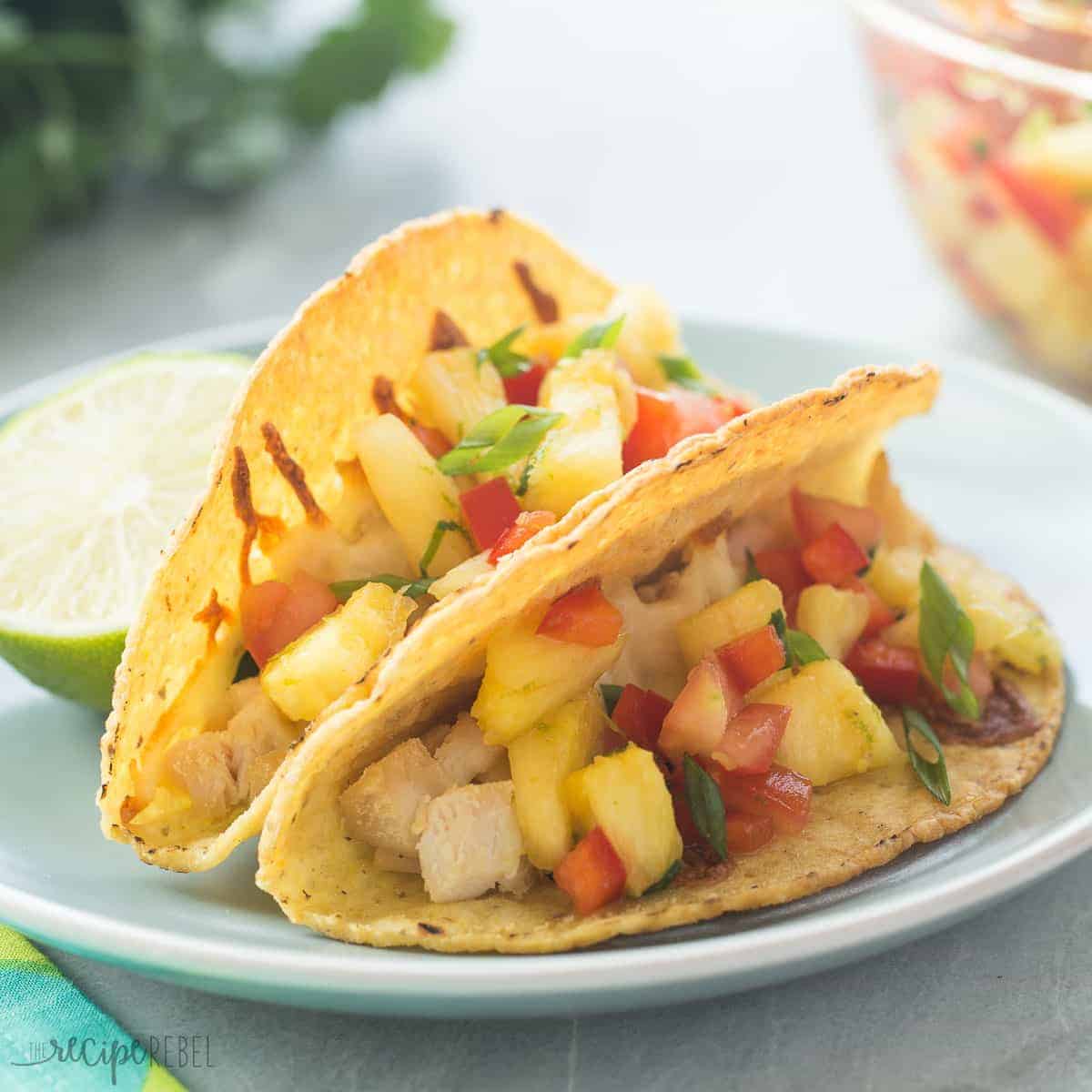 close up image of chicken tacos with pineapple salsa on blue plate with lime half in the background
