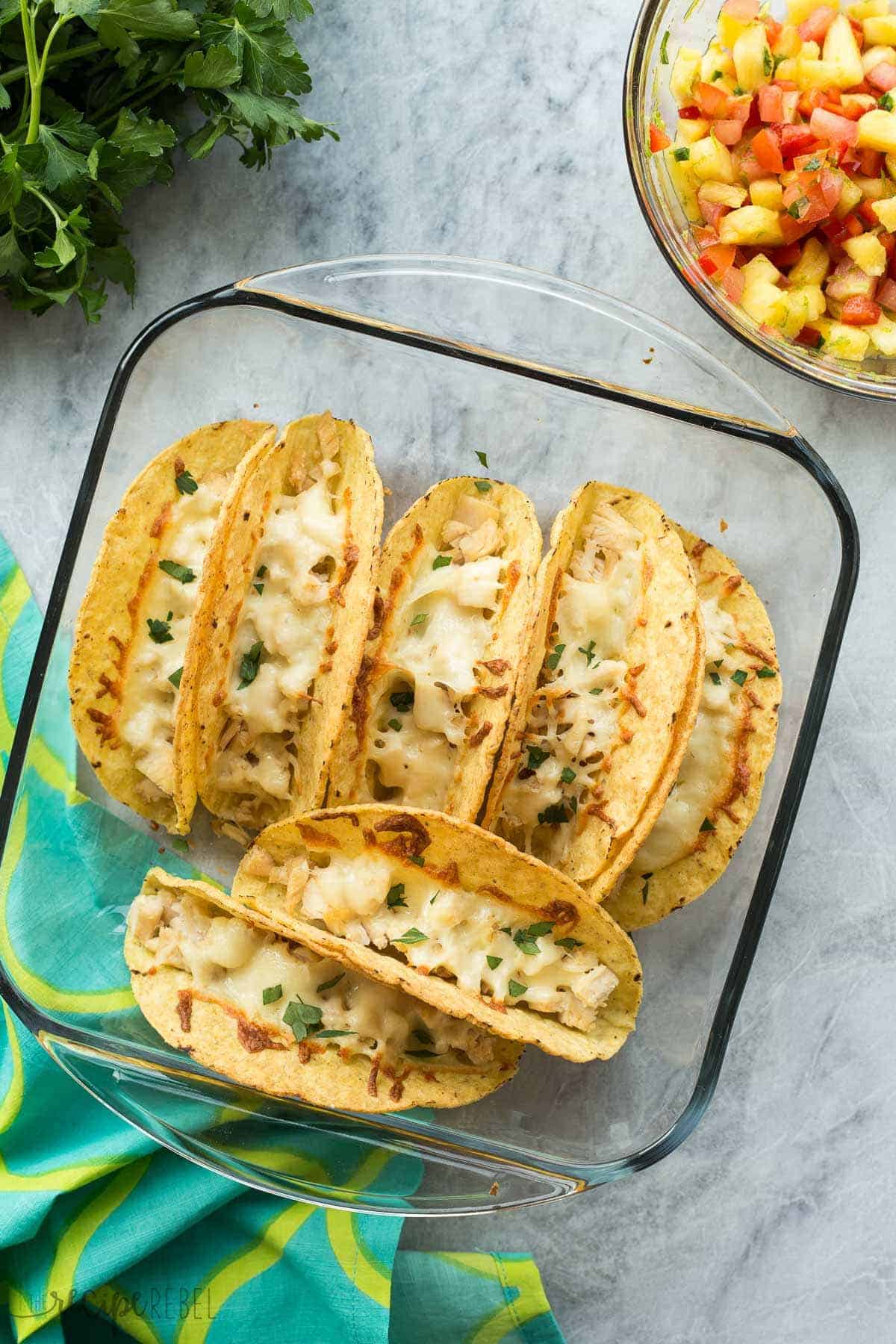 overhead image of baked chicken tacos in glass pan with pineapple salsa on the side