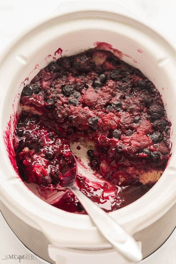 This Slow Cooker Berry Cobbler is an easy dessert recipe that uses fresh or frozen berries so it's the perfect sweet treat year round! Just 10 minutes prep! #berries #dessert #slowcooker #crockpot slow cooker berry cobbler in white crockpot with scoop missing