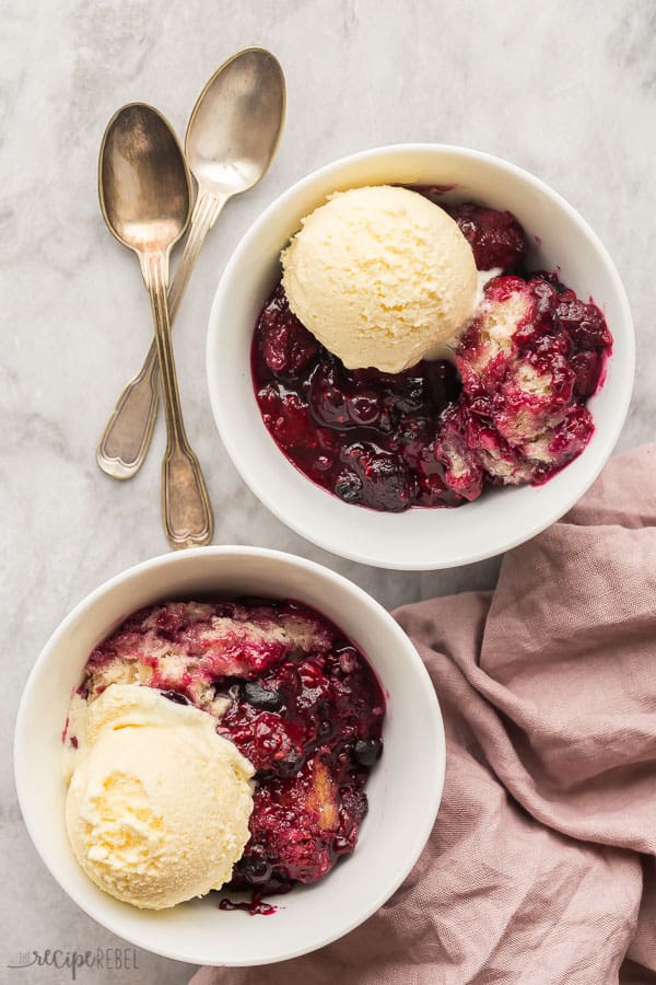 two bowls of slow cooker berry cobbler with ice cream scoops and pink towel