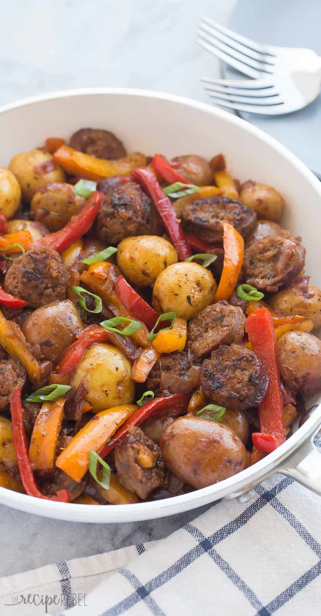 sausage potato and peppers skillet in white pan with green onions