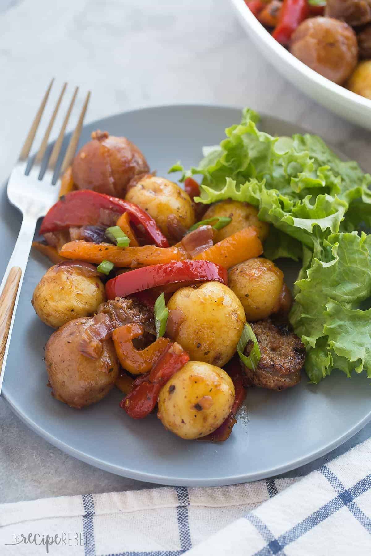 grey plate with sausage potatoes and peppers in barbecue sauce with fresh greens on the side