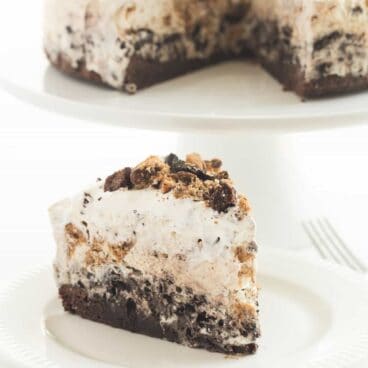 The ULTIMATE Ice Cream Cake! A brownie base topped with a no churn Oreo ice cream layer, fudge crumbles, a Chocolate Chip Cookie ice cream layer, then covered in whipped cream!