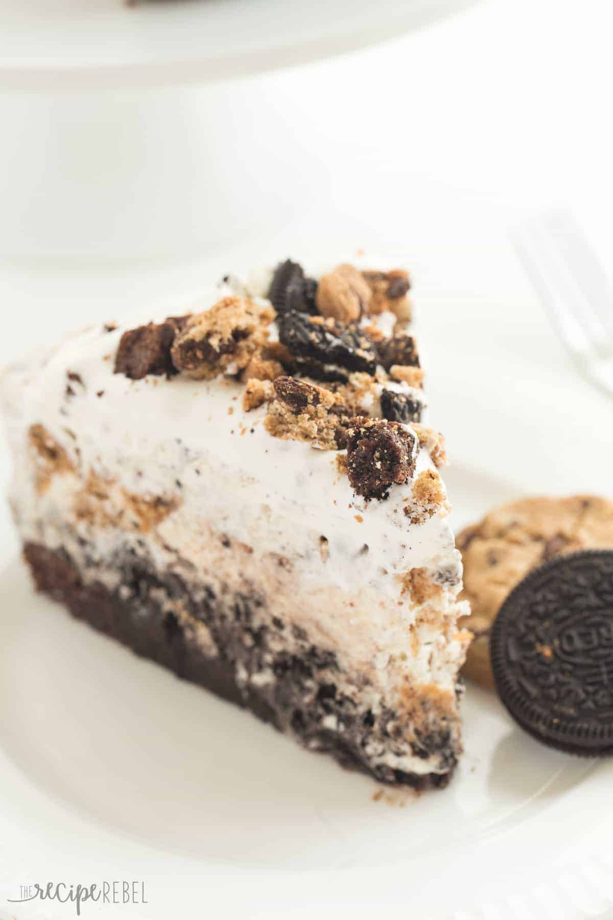 the ultimate ice cream cake slice on white plate with crumbled cookies oreos and brownies