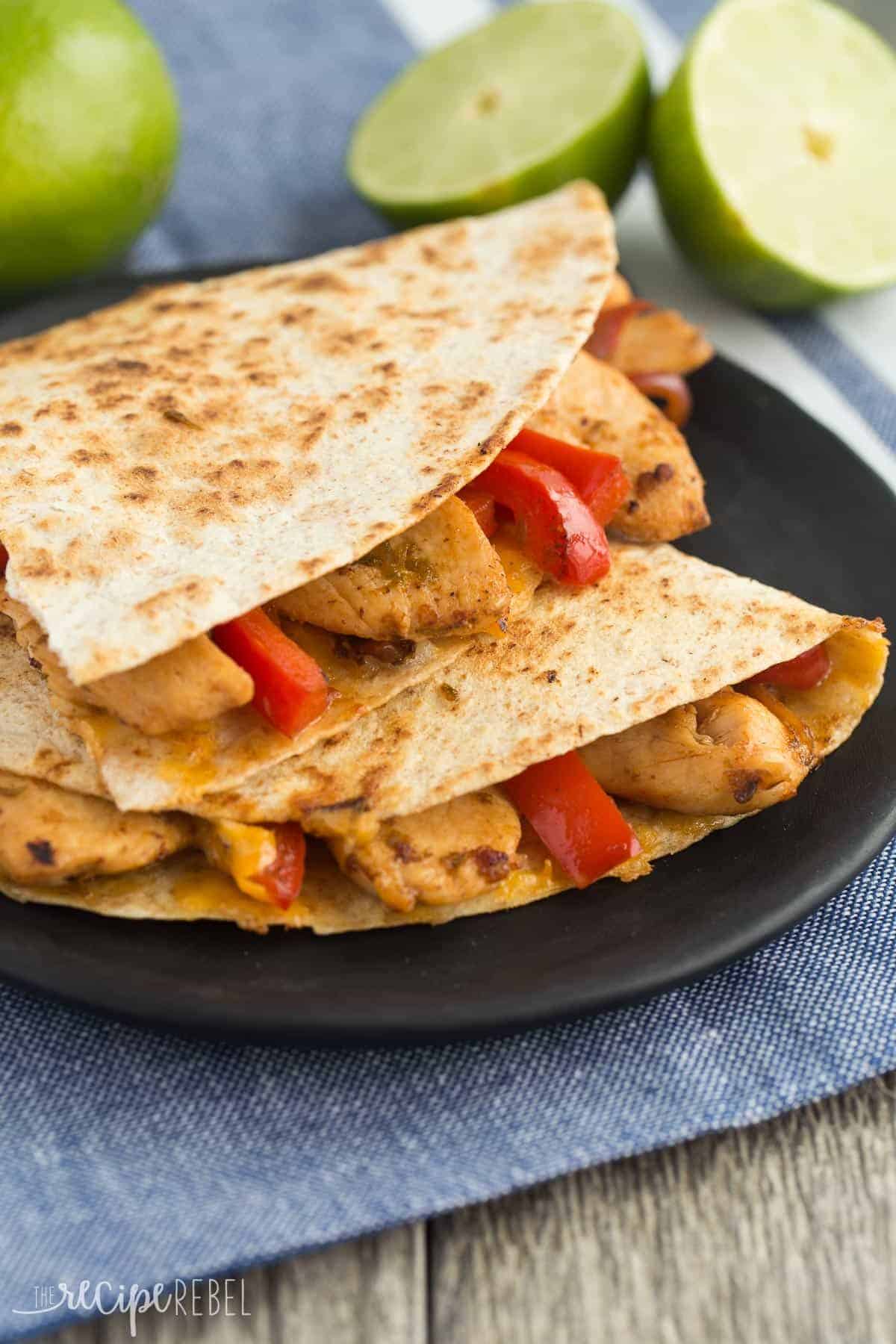 honey lime chicken quesadillas on a black plate with red peppers and lime halves in the background