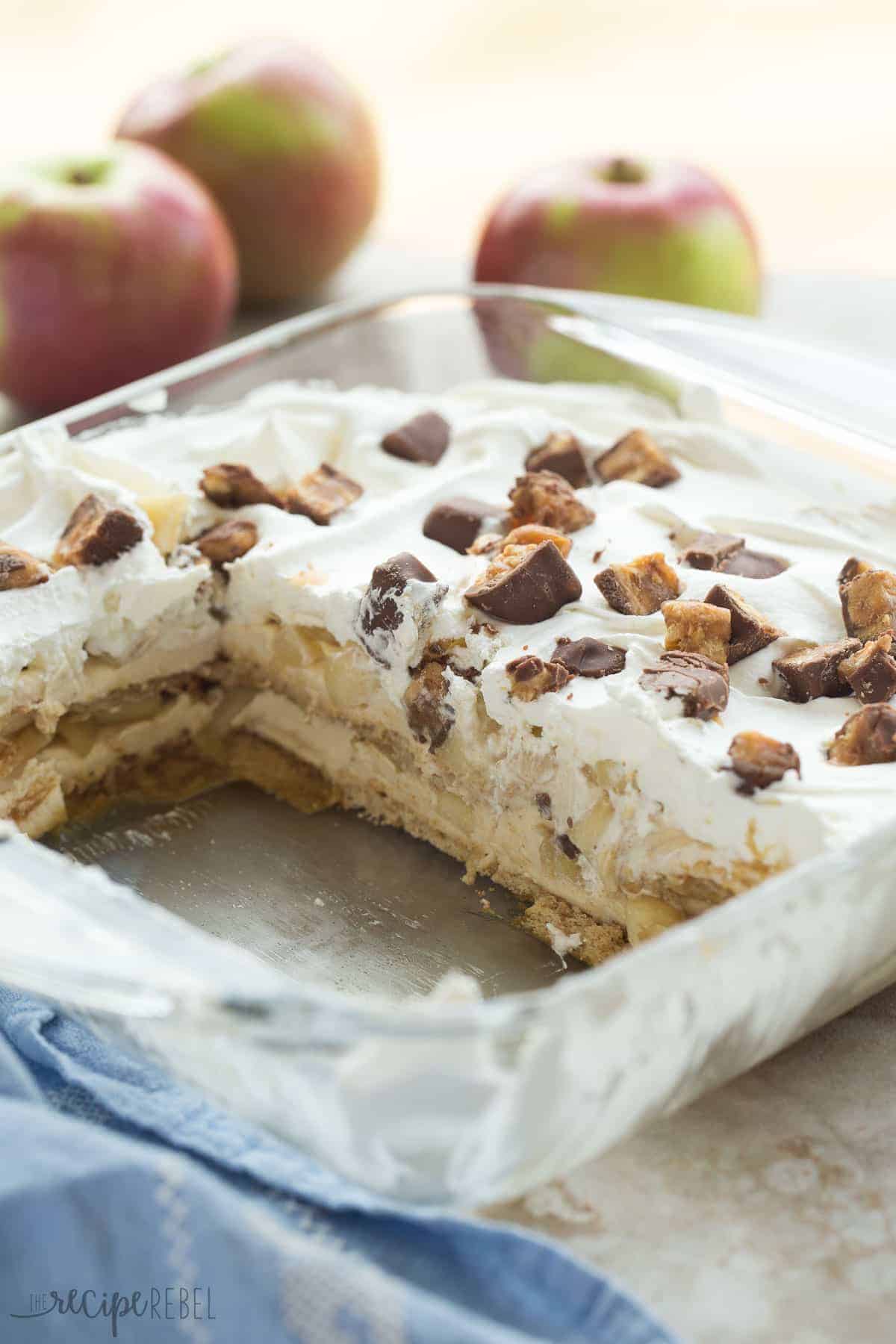 clear baking dish with snickers apple icebox cake with two pieces cut out
