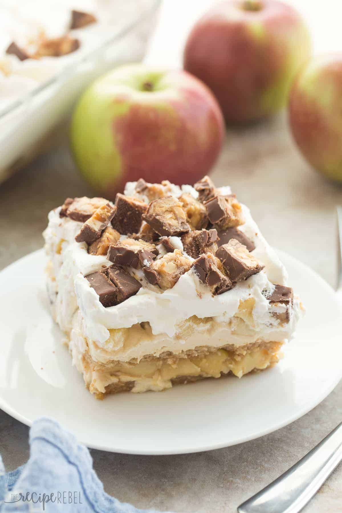 snickers apple icebox cake piece on white plate with whole apples in the background