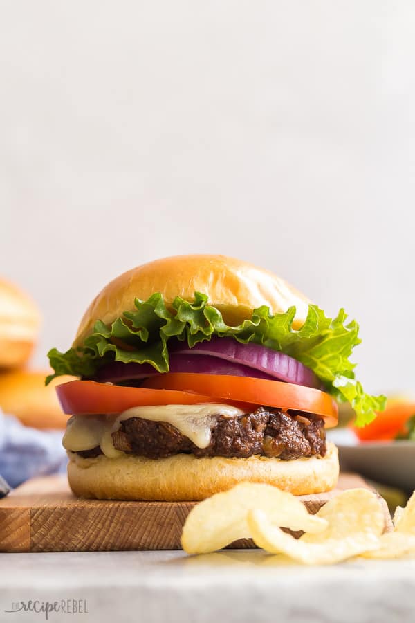 close up of burger on wooden board with chips on the side