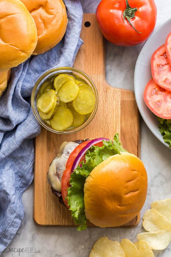 These are the BEST Burgers! Made with a mix of ground beef and ground pork, caramelized onions, balsamic vinegar, chili powder and MORE that makes them so much more flavorful than other burgers! #burger #hamburger #grilling #recipe #dinner overhead image of burgers and pickles son wooden platter with toppings on the side
