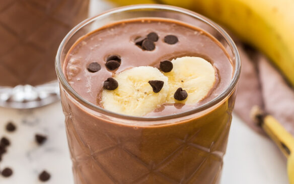 two glasses of chocolate peanut butter smoothie with bananas in the background